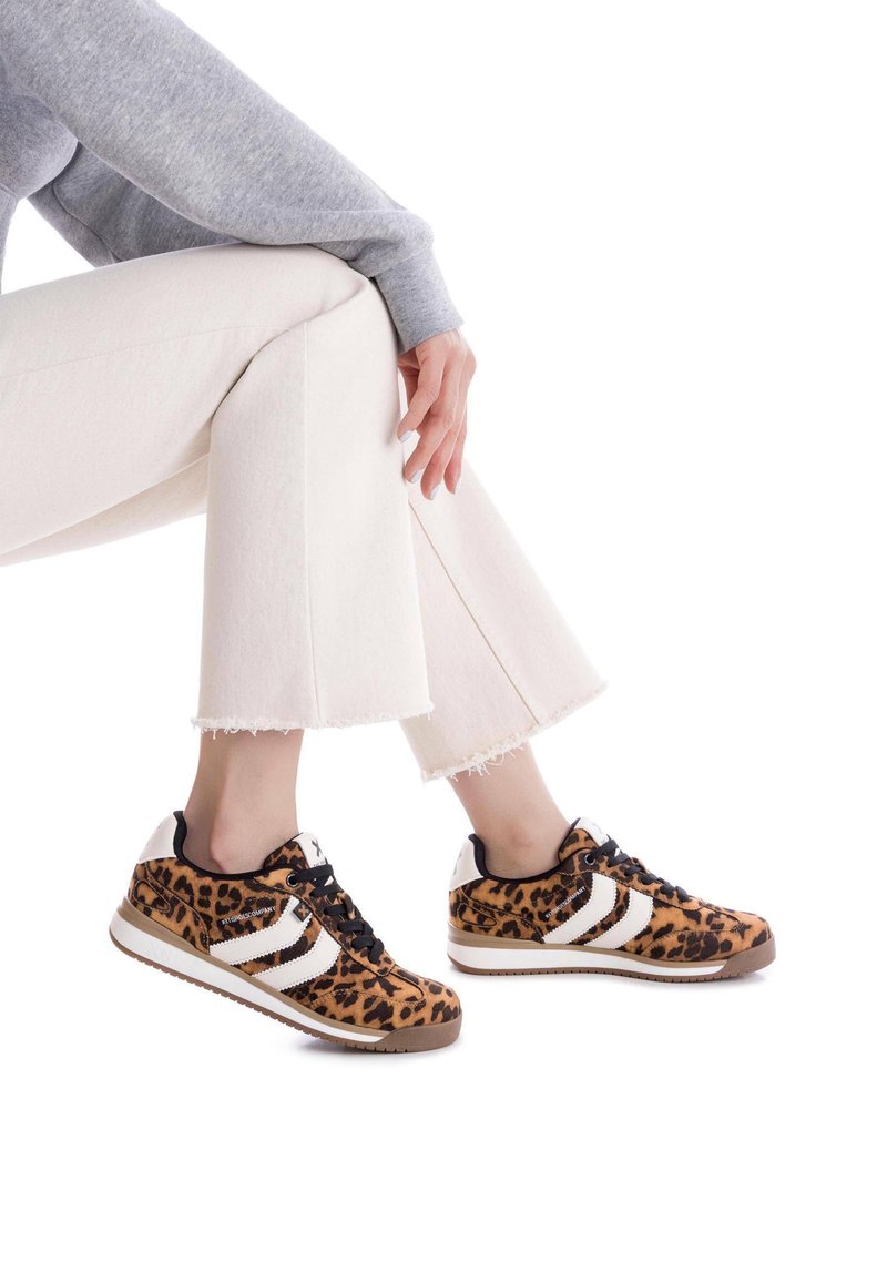 Las zapatillas de leopardo presentan un material similar a piel en tonos marrones y negros con rayas blancas, cordones negros, acentos blancos y una suela de goma texturizada.