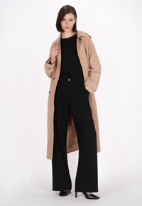 Palton bej cu un design dublu-breasted, top negru și pantaloni largi negri cu talie înaltă, completat cu pantofi cu toc ascuțit negri.