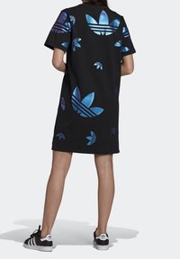 Svart oversized t-shirt klänning med reflekterande blå Adidas logotypmönster. Bärs med svarta och vita Adidas sneakers med tre ränder.