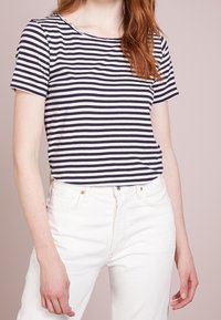 Marinblå och vita randiga t-shirt med rund halsringning och korta ärmar, matchad med vita högmidjade jeans. Mjuk bomullstyg.