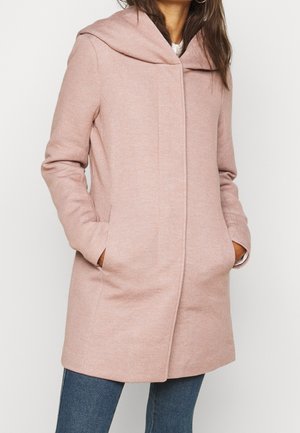 Cappotto in misto lana di un leggero rosa con cappuccio ampio e ripiegato, maniche lunghe e due tasche laterali. Presenta una linea dritta e cuciture minime.