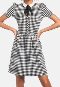 Musta-valkoinen ruudullinen mekko, jossa on lyhyet puffihihat, valkoinen kaulus, napit edessä ja laskostettu hame.