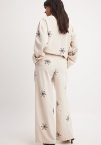 Krämlinned tvådelat outfit med svart blommönster. Består av en löst sittande skjorta och vida byxor som visar upp en luftig textur.