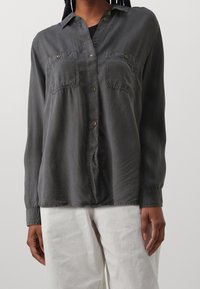 Grå långärmad skjorta i mjukt tyg, med två bröstfickor, knappstängning fram och krage. Strukturerad yta med en avslappnad passform.