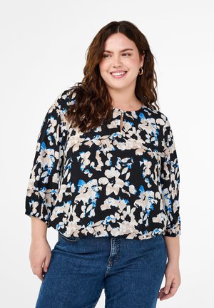 Blouse florale noire, ornée de motifs beiges et bleus, avec un col rond et un détail en forme de trou de serrure, et des manches trois-quarts. Associée à un jean bleu.
