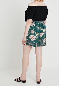 Svart off-shoulder topp i kombination med gröna blommiga shorts med rosa och vita blommor, elastisk midja och svarta slip-on sandaler.