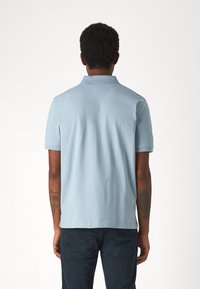 Polo shirt azzurro chiaro a maniche corte con colletto classico e orlo dritto. Realizzato in un tessuto morbido con una trama liscia. Jeans visibili sotto.