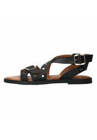 Zwarte leren sandaal met een open ontwerp, voorzien van metallic studs en een gespsluiting over de tenen, gezet op een vlakke bruine zool.