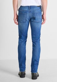Jeans in denim blu con una vestibilità slim, tasche posteriori standard e una vita a media altezza, abbinati a stivali neri alla caviglia.