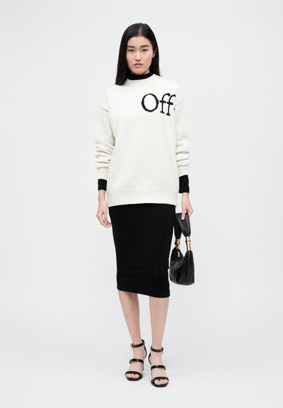 Λευκό oversized πουλόβερ με γραφικό "Off", μαύρη ε fitted μίντι φούστα, μαύρες strappy γόβες και μικρή μαύρη τσάντα. Λείες υφές, στιλάτη αντίθεση.