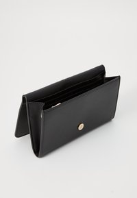 Portefeuille en cuir noir au design structuré, avec une fermeture à pression dorée et plusieurs emplacements pour cartes, mettant en avant une texture lisse.