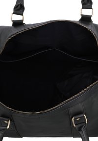Offene schwarze Ledertasche mit goldenem Reißverschluss und schwarzem Innenfutter, die ein geräumiges, leeres Hauptfach und zwei schwarze Griffe mit goldener Beschläge zeigt.