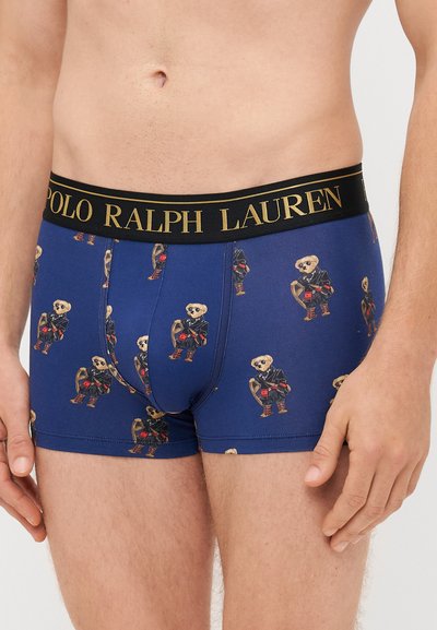Bóxer azul con un patrón de osos de dibujos animados que llevan un abrigo negro. Presenta una cintura negra con "POLO RALPH LAUREN" en letras doradas.