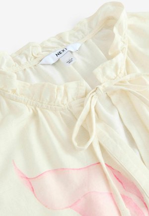 Blouse en crème clair avec un col à volants et une fermeture à nouer. Présente une texture douce et un motif abstrait rose subtil à l'avant.