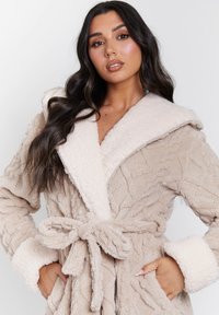 Beige badjas met een gestructureerde buitenlaag, zachte crèmekleurige kraag en manchetten, strikceintuur en zijzakken. Comfortabel fleecemateriaal.