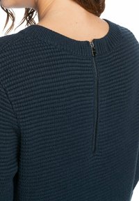 Pull bleu marine tricoté avec un motif côtelé texturé et une fermeture éclair au dos allant de l'encolure à l'ourlet.