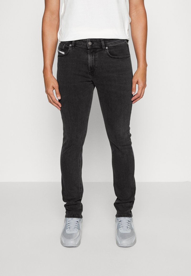 Jeans slim fit negros de tejido de mezclilla con cinco bolsillos, cierre de botón metálico y ligero desvanecimiento. Combinados con zapatillas deportivas gris claro.