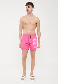 Costumi da bagno rosa con un motivo floreale sul lato sinistro, dotati di un laccio nero e di una texture leggera e liscia.