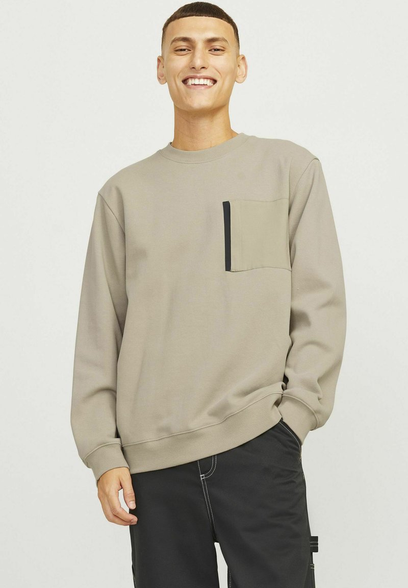 Sweatshirt kaki avec col rond, manches longues et poche poitrine avec un bord noir. Texture douce et coupe décontractée.