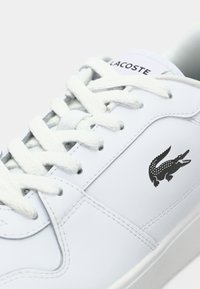 Baskets en cuir blanc avec lacets blancs, avec un logo crocodile noir et le texte "LACOSTE" sur la languette.