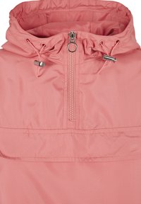 Giacca leggera con cappuccio di un delicato rosa pallido, con chiusura a mezza zip sul davanti, cordoncino regolabile sul cappuccio e una texture liscia e opaca.