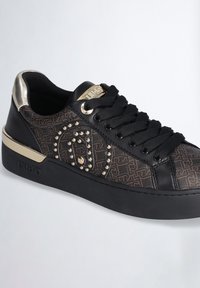 Sneaker nera con una tomaia in tessuto a fantasia, dettagli dorati, applicazioni in metallo e una suola nera spessa. Lacci piatti e un logo metallico sulla linguetta.