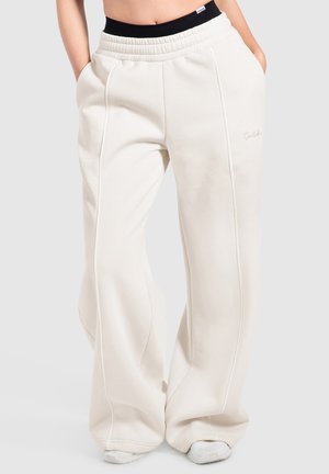 Løse hvide joggingbukser med synlige sømme og sidelommer, båret med synlig sort linning og hvide sneakers under.