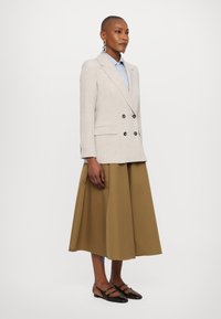 Beige dobbeltspent blazer, blå stripete skjorte, olivengrønn A-linje skjørt og svarte leiligheter med stropper. Strukturert stoff og skreddersydd passform.