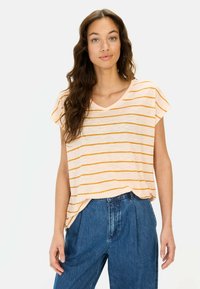 Korte mouwen, V-hals top in lichtbeige met oranje horizontale strepen; gecombineerd met hoge taille blauwe denim broek. Zachte textuur.