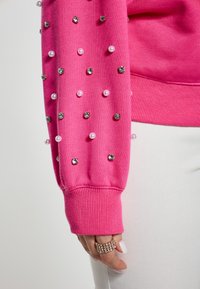 Manga de sudadera en rosa brillante con perlas decorativas y piedras de imitación, puño acanalado y una textura de algodón suave.