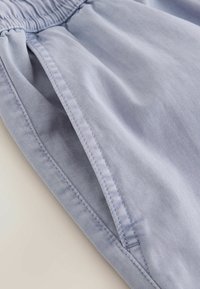 Tissu bleu clair avec une poche cousue et une taille élastique, montrant la texture et les détails des coutures d'un vêtement.