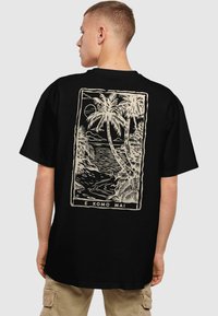 Sort kortærmet t-shirt med et cremafarvet grafik af palmer og en kystlinje med teksten "E KOMO MAI" nederst.