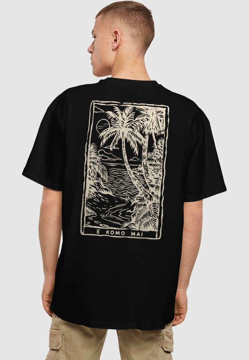 Sort kortærmet t-shirt med et cremafarvet grafik af palmer og en kystlinje med teksten "E KOMO MAI" nederst.