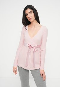 Top cruzado de manga larga color rosa claro con escote en V profundo y una cinta de raso rosa atada en la cintura, combinado con leggings grises.