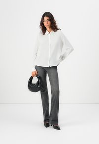 Camicia bianca a maniche lunghe con taglio dritto, abbinata a jeans grigi a zampa d'elefante. Tiene una borsa nera in tessuto. Scarpe nere a punta.