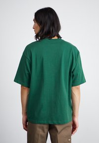 Grøn bomulds t-shirt med en afslappet pasform, rund halsudskæring og korte ærmer, vist fra ryggen. Glat tekstur, ingen synlige mønstre.