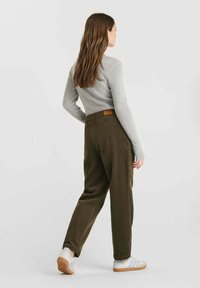 Olive green corduroy pants, relaxed fit, textured material, paired with a light gray ribbed sweater and white sneakers with gum soles.