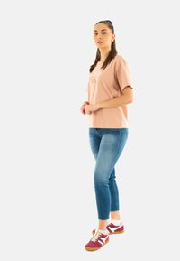 Camiseta de algodón rosa claro con un ajuste holgado, combinada con jeans ajustados azul y zapatillas burdeos con rayas blancas y una suela texturizada.