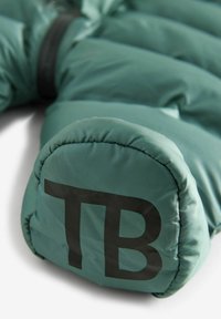 T�õemefli kaasaegne teal värvi pufferjakk, millel on tikandmustrit, ümar õlgade kujundus ja silmatorkav must "TB" logo. Nähtavad tõmbluku detailid.