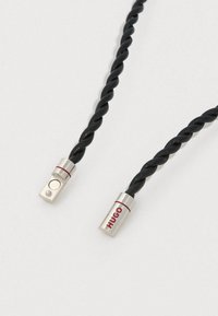 Sort snoet snor med sølvfarvede ender med indgraveret 'HUGO' logo og en rød accentlinje. Glat tekstur, minimalistisk design.