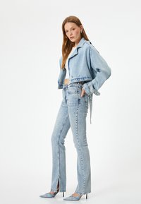 Chaqueta de mezclilla azul claro con un diseño cortado y botones en la parte delantera, combinada con unos pantalones rectos de color similar que tienen dobladillos cortados.