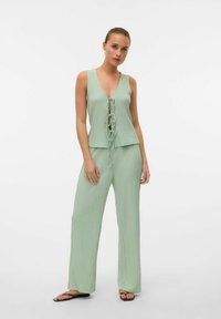 Completo a due pezzi verde chiaro composto da un top senza maniche con scollatura a V e dettaglio a fiocco, abbinato a pantaloni a gamba larga in un tessuto testurizzato.