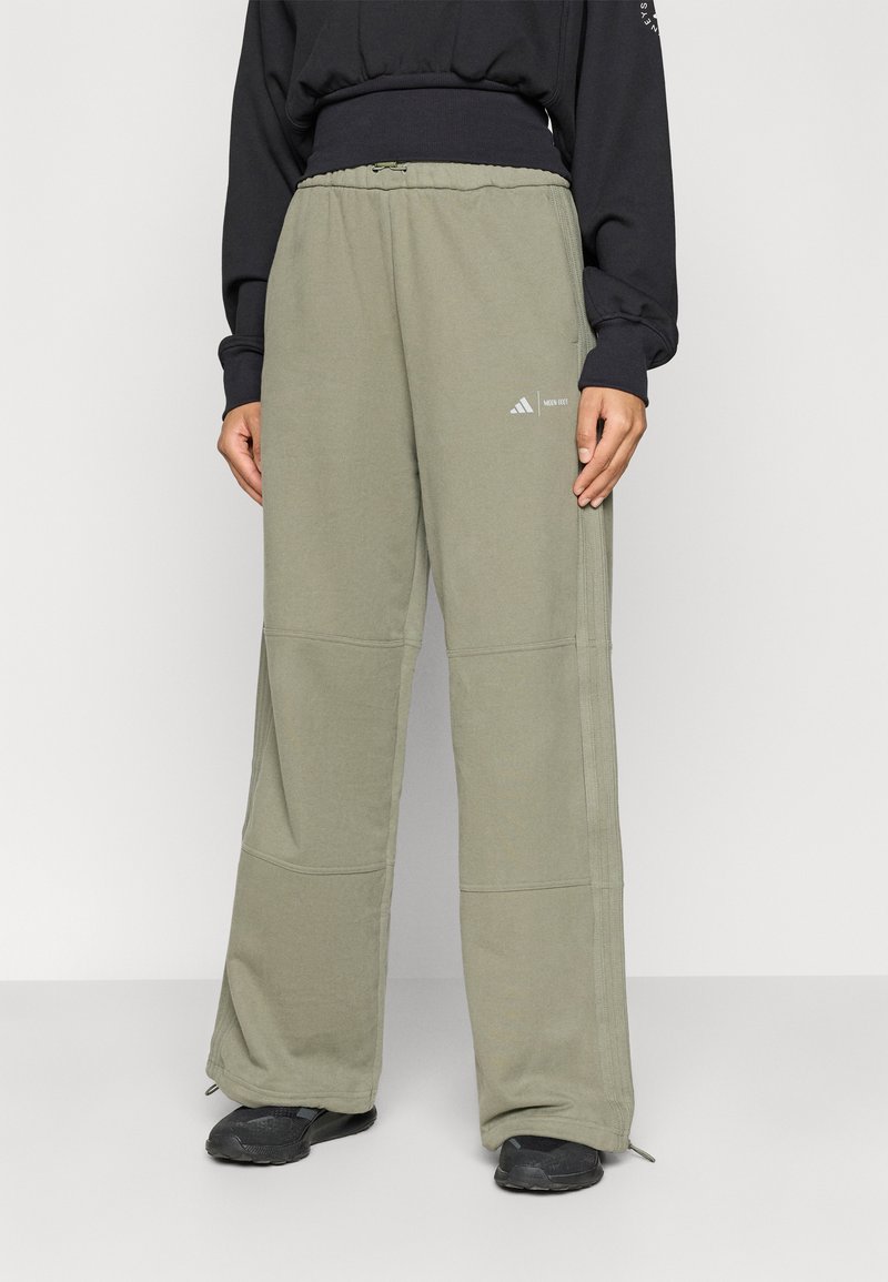 Persoon gekleed in losse, olijfgroene wijde broek met elastische taille en een klein wit logo op de bovenbeen, gecombineerd met zwarte sneakers en een zwart topje.