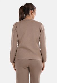 Giacca beige a maniche lunghe realizzata in tessuto morbido con una vestibilità dritta e colletto piatto. Texture liscia, presenta un design semplice e senza cuciture.