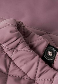 Nafialovkastofovaná látka so zvýraznenými stehmi a priehľadným plastovým gombíkom prišitým zhodnou niťou na čiernom látkovom štítku.