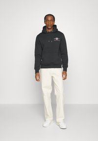 Sort hætte sweatshirt med en frontlomme og et grafisk logo. Parret med hvide lige bukser og hvide sneakers.