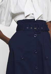 Gonna blu navy con vita alta, ampia cintura e chiusure con bottoni, dotata di tasche laterali e una trama liscia e strutturata.