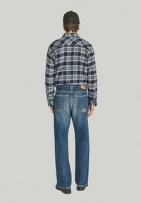 Camicia di flanella a quadri blu con colletto button-down, abbinata a jeans dritti in lavaggio chiaro con tasche posteriori e etichetta in pelle.