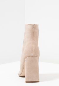 Botines de ante beige con tacón alto cónico, diseño ajustado al tobillo y construcción sin costuras. Textura suave sin adornos.