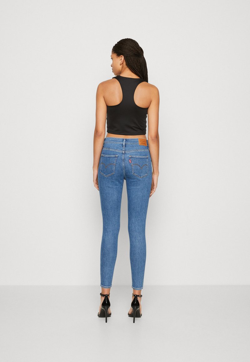 Hoch geschnittene, blaue Denim-Skinny-Jeans mit glatter Textur und fünf Taschen, kombiniert mit einem schwarzen ärmellosen Cropped-Top. Quadratförmiger Ausschnitt im Rücken.